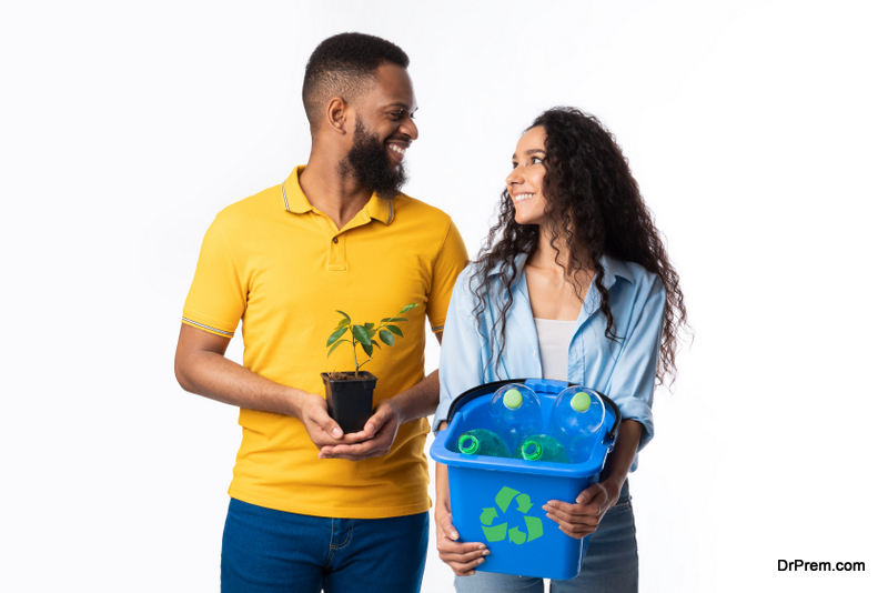  Cheerful Diverse Couple Holding Plant And Bucket With Recycling Waste And Plastic Bottles Smiling Each Other 